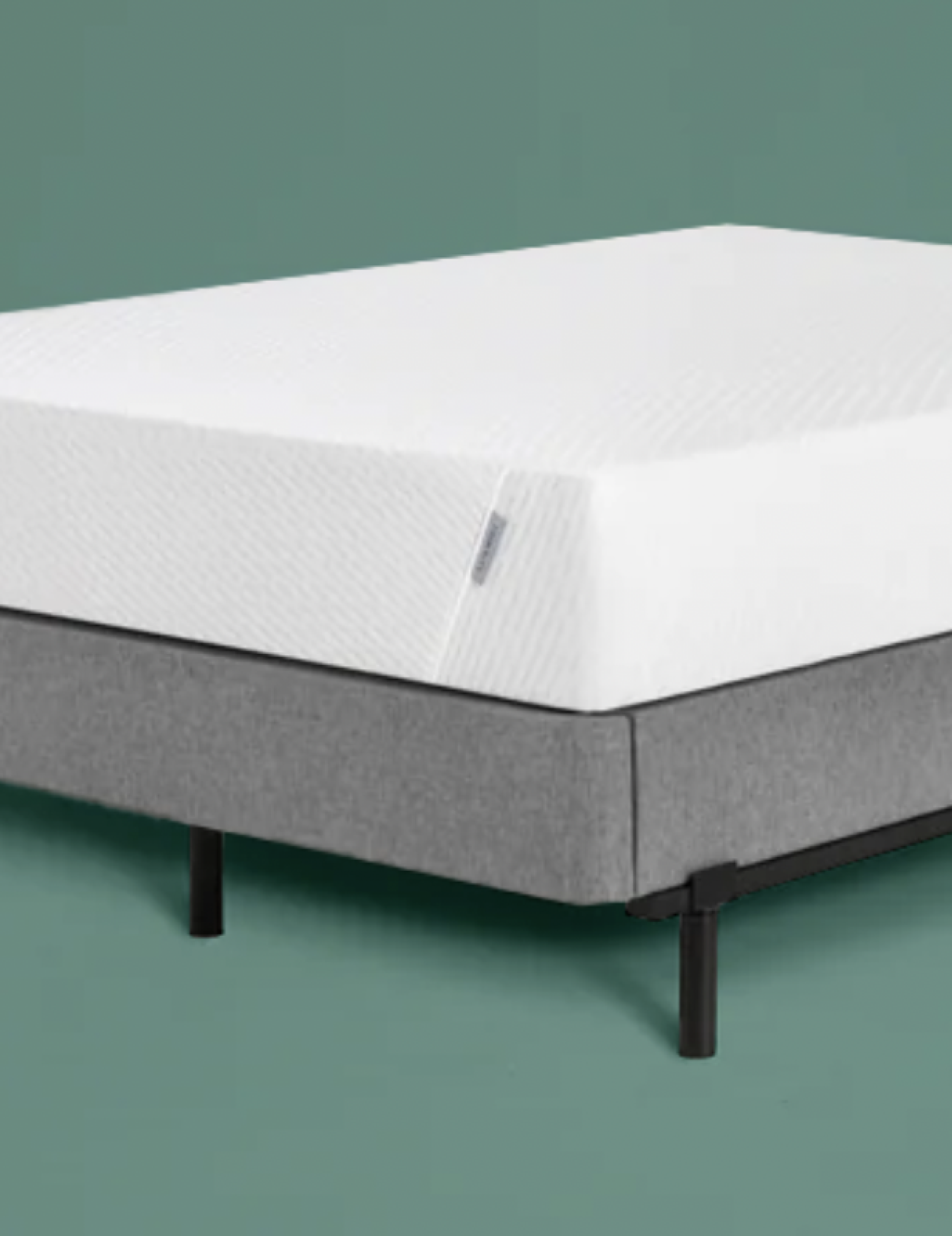 Tuft & Needle mattress on a gray upholstered platform bed frame against a green wall.