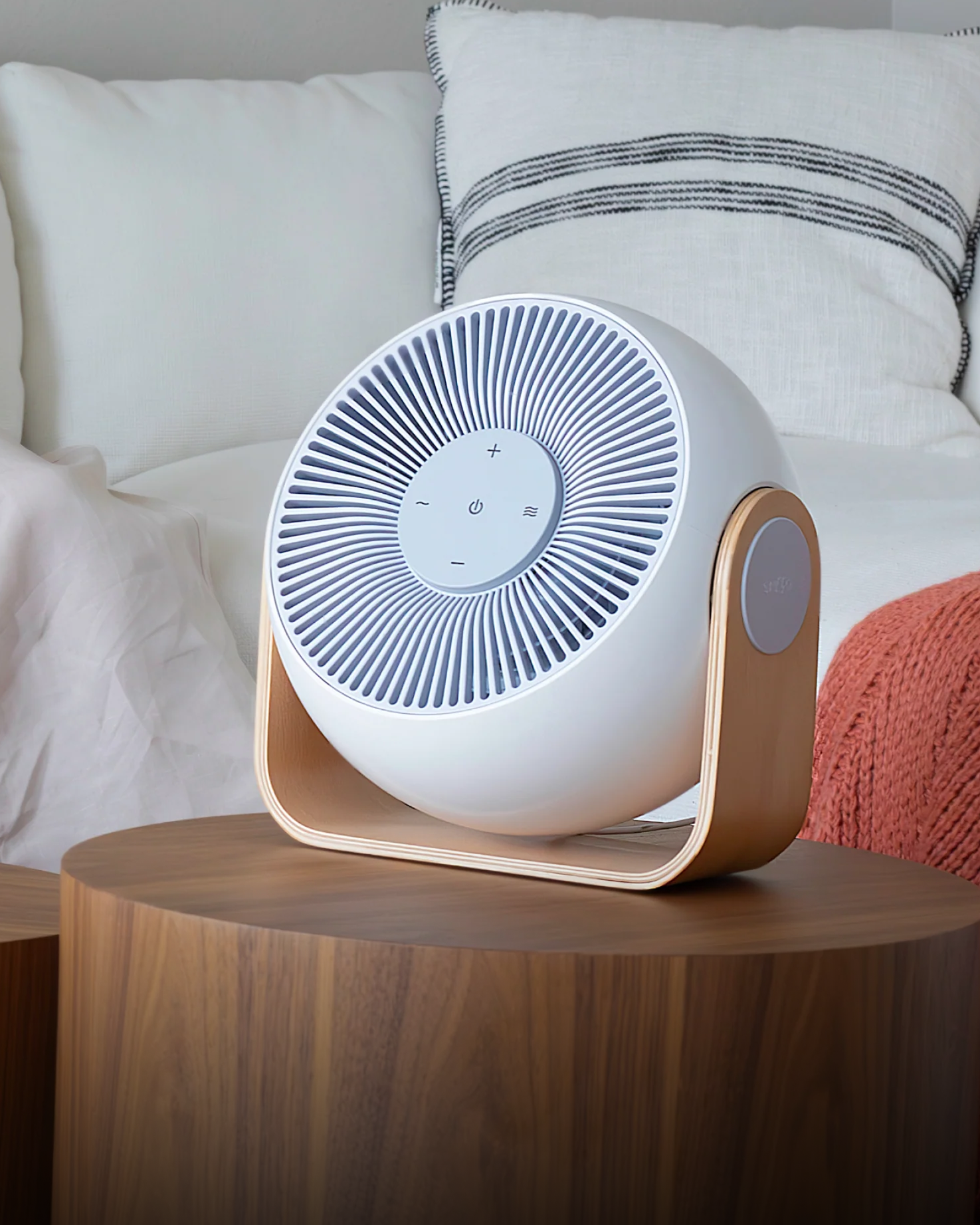 White circular fan-style sleep device with wooden legs on a round wooden table in front of white bedding.